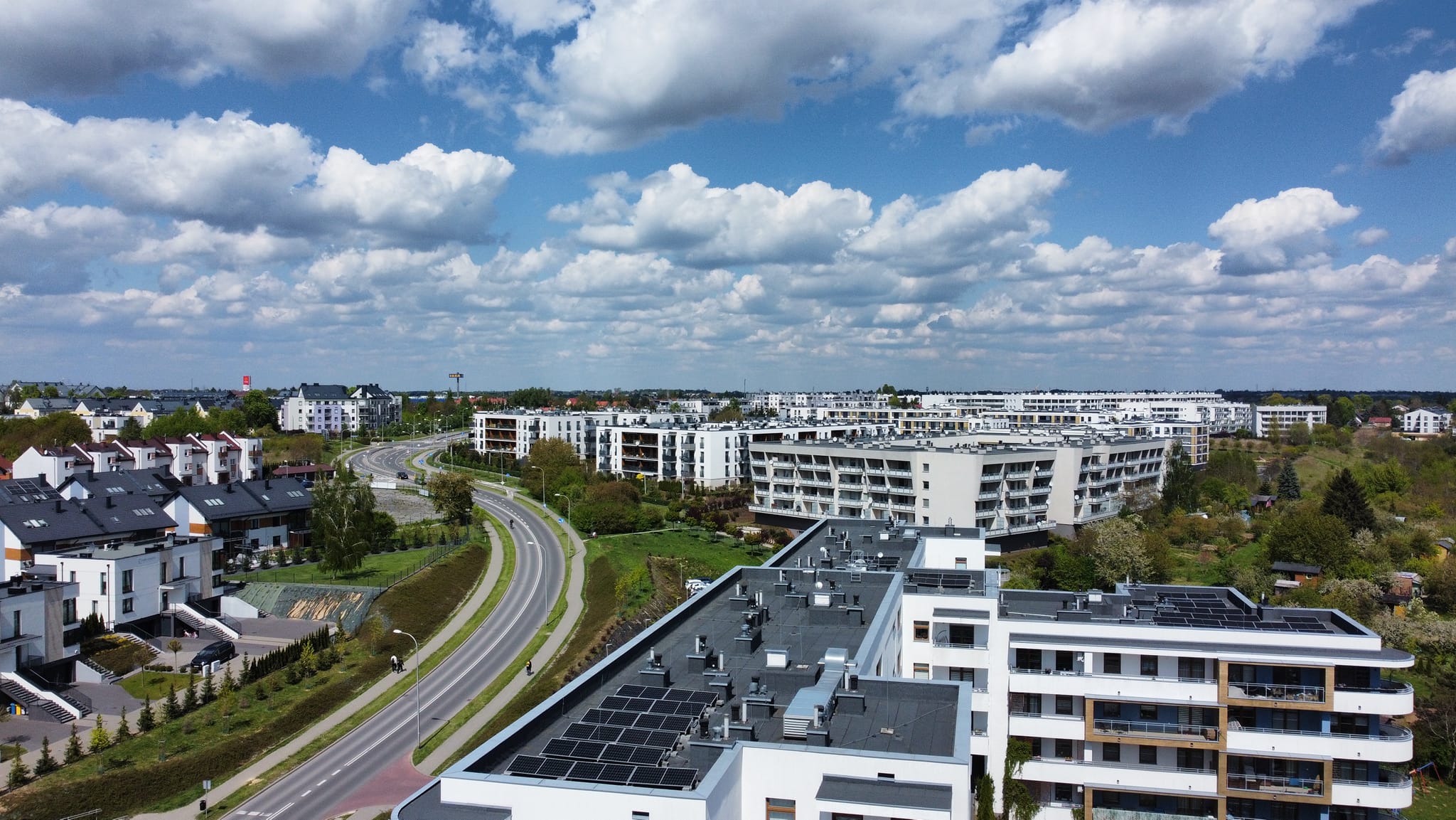 Widok z lotu ptaka na nowoczesne osiedle mieszkaniowe z panelami fotowoltaicznymi na dachach budynków.